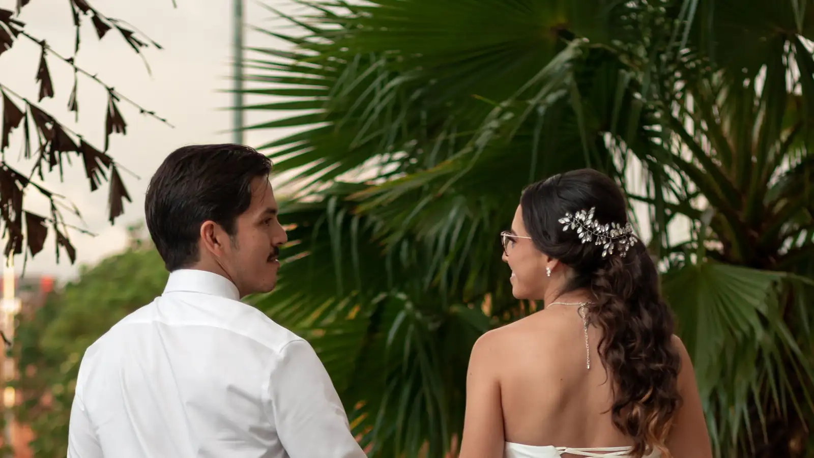 Novios de espaldas caminando de la mano entre palmeras