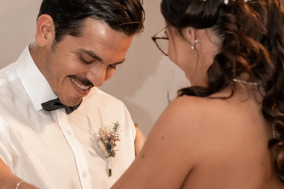 Novios riendo juntos durante su boda, él con moño y ella con flores en el cabello