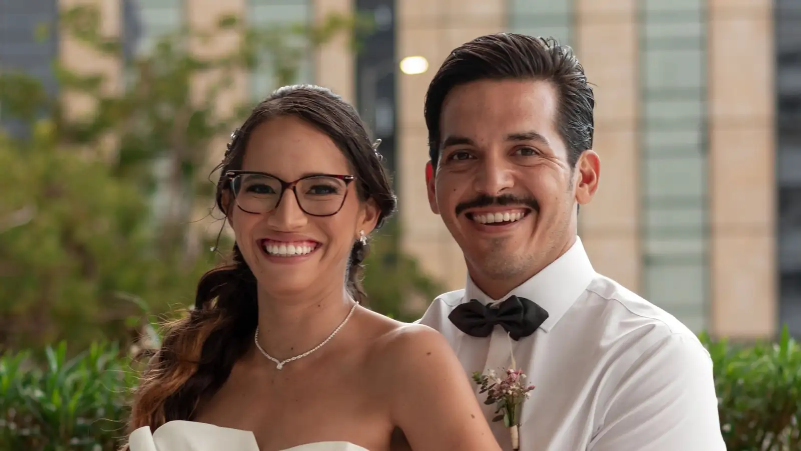 Novios abrazados sonriendo a la cámara, él detrás de ella