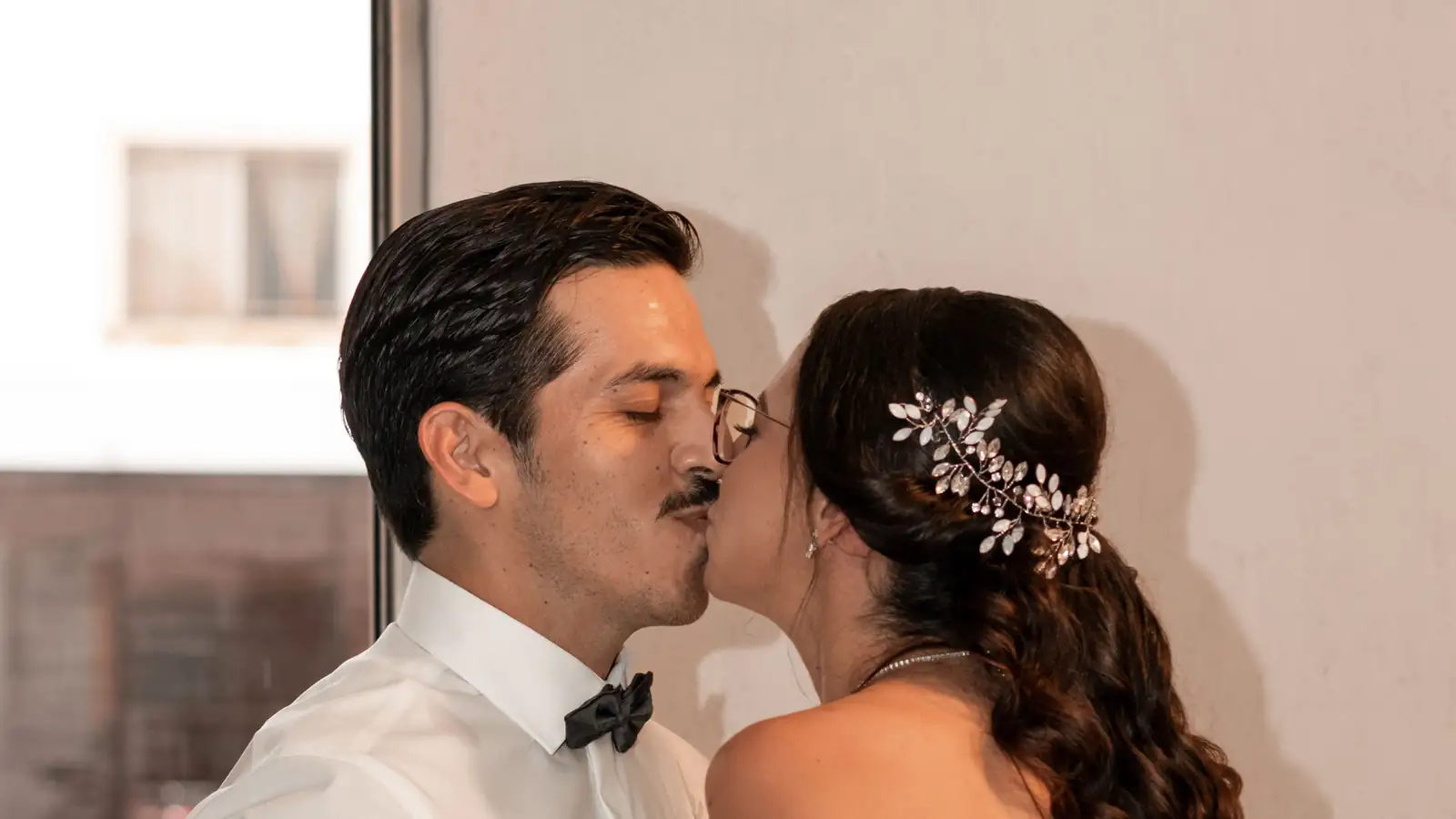 Novio dándole un beso a la novia, que cierra los ojos, con un tocado de flores en el cabello
